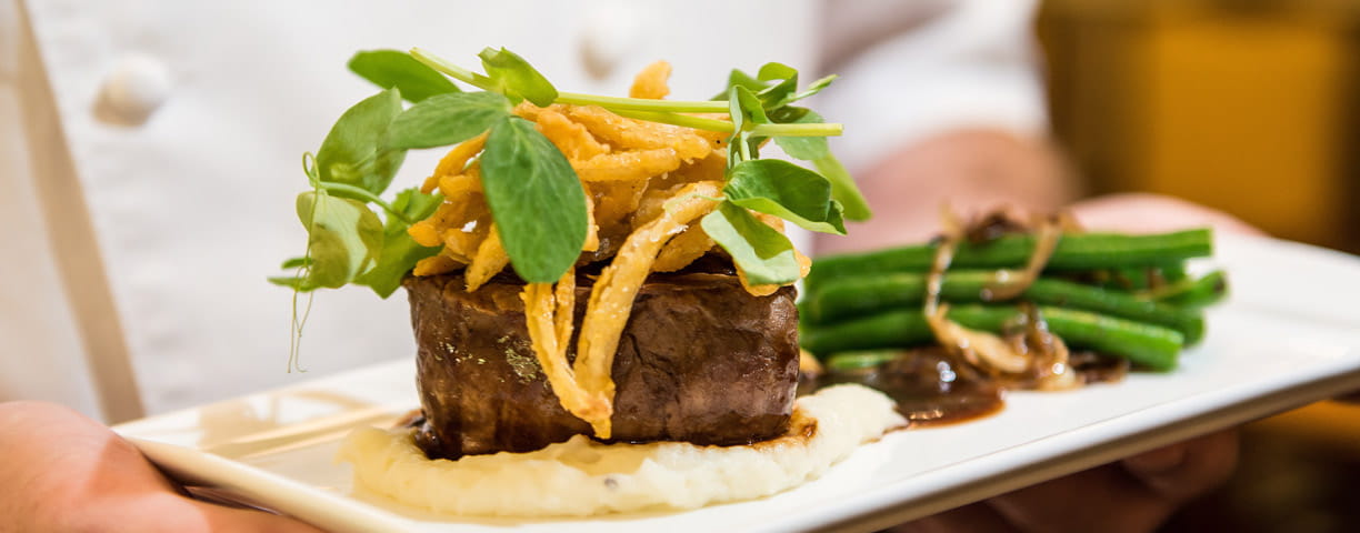A chef holds a plate of steak with potatoes and asparagus.