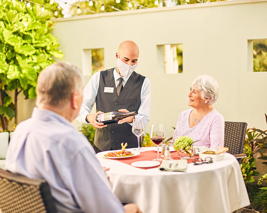 A couple dines outdoors at Vi while a masked waiter pours wine