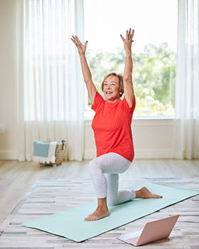 A resident does yoga while watching instruction on her laptop